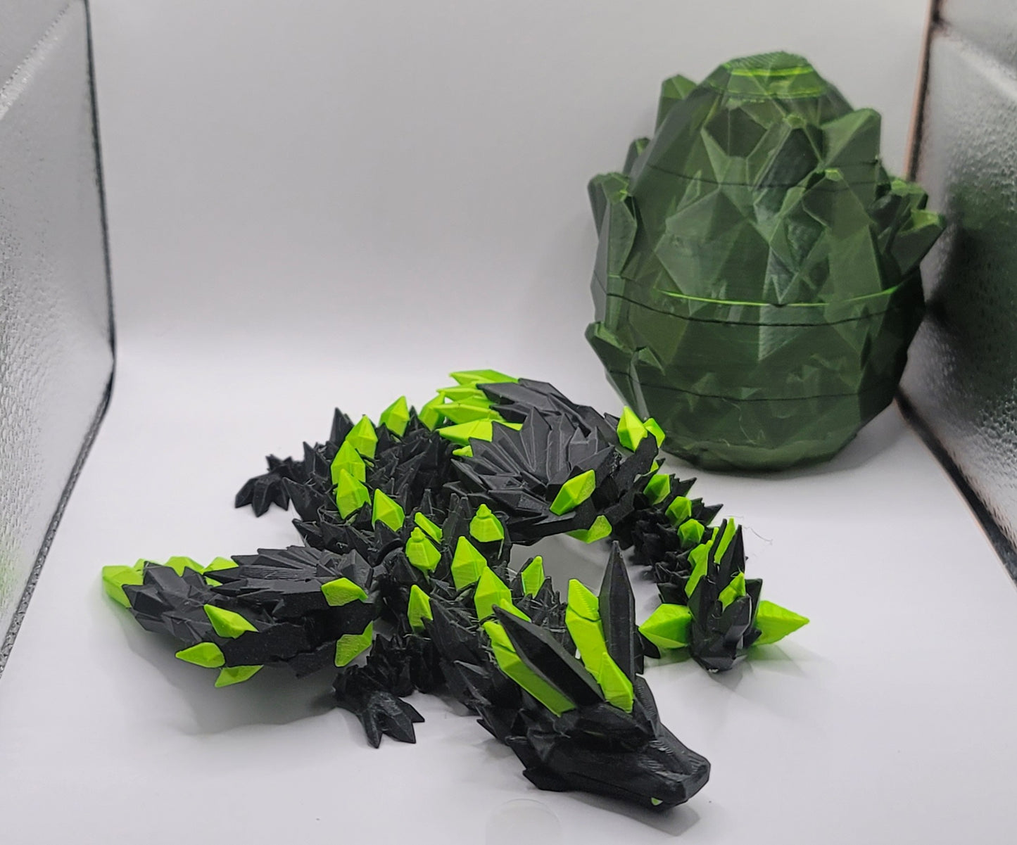 Black and green 3D printed Crystal Adult Dragon figurine posed next to matching green dragon egg